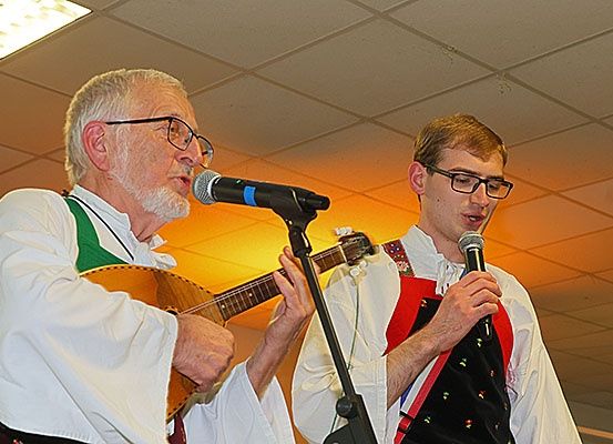 Zwei Musiker, einer spielt eine Laute und der andere singt, treten mit einem Mikrofon auf der Bühne auf.