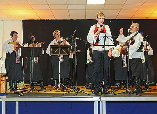 Eine Band tritt auf der Bühne auf. Ein Mann singt in ein Mikrofon. Andere spielen Gitarren. Sie tragen traditionelle Kleidung. Die Bühne hat einen schwarzen Hintergrund und einen blauen Boden.