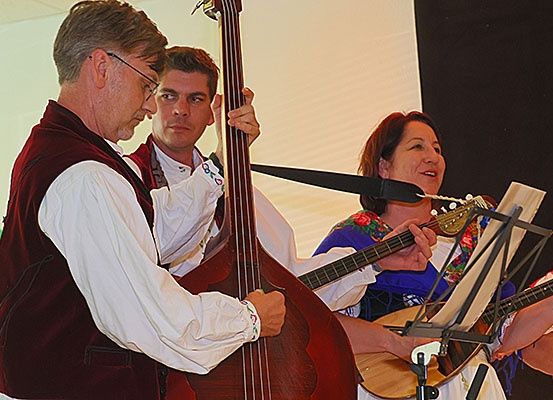 Drei Musiker treten auf der Bühne auf. Ein Mann spielt den Bass, während eine Frau die Gitarre spielt. Ein anderer Mann schaut zu, und ein Mikrofon ist in der Nähe.