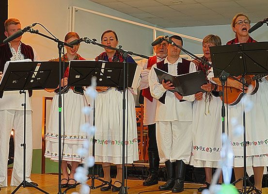 Eine Gruppe von Musikern in traditioneller Kleidung tritt auf der Bühne auf, wobei Frauen singen und Notenständer halten und Männer Gitarren spielen.