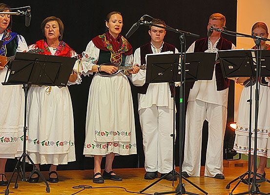 Eine Gruppe von Menschen in traditioneller Volkskleidung tritt auf der Bühne auf, spielt Instrumente und singt.