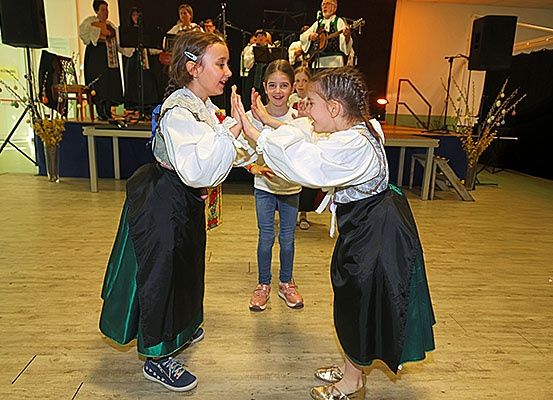 Zwei junge Mädchen tanzen auf der Bühne in traditionellen Kostümen, während eine Band hinter ihnen spielt.