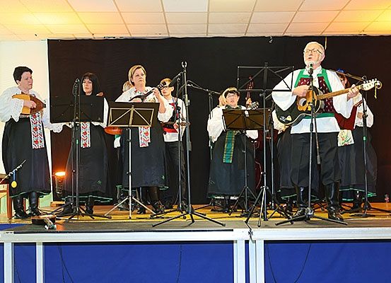 Eine Gruppe Musiker in traditioneller Kleidung spielt auf der Bühne und verwendet verschiedene Instrumente, darunter Gitarren und Flöten.