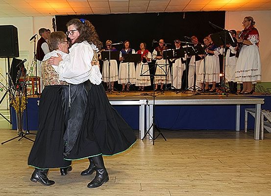 Zwei Personen tanzen auf einer Bühne, während eine Gruppe von Musikern im Hintergrund Instrumente spielt.