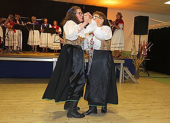 Zwei Frauen in traditioneller Kleidung tanzen auf der Bühne, während eine Band im Hintergrund spielt.