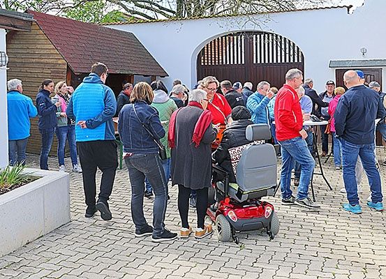 Eine Gruppe von Menschen versammelt sich um einen Tisch auf einem Innenhof, wobei eine Frau einen Rollstuhl benutzt, und sie scheinen in ein Gespräch vertieft zu sein.