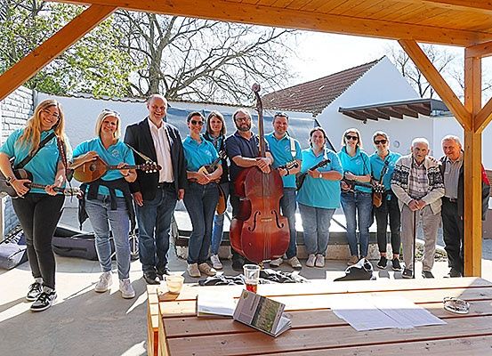 Eine Gruppe von Menschen in blauen Shirts steht und posiert mit ihren Instrumenten in einem Pavillon für ein Foto.