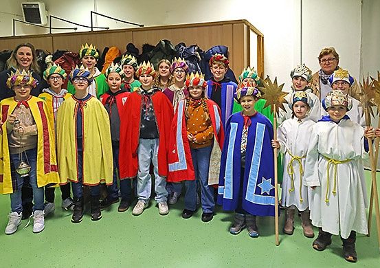 Eine Gruppe von Kindern in farbenfrohen Kostümen und mit Requisiten, posiert mit Lehrern in einem Raum für ein Foto.