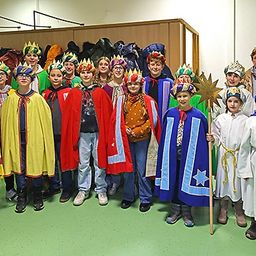 Eine Gruppe von Kindern in farbenfrohen Kostümen und mit Requisiten, posiert mit Lehrern in einem Raum für ein Foto.