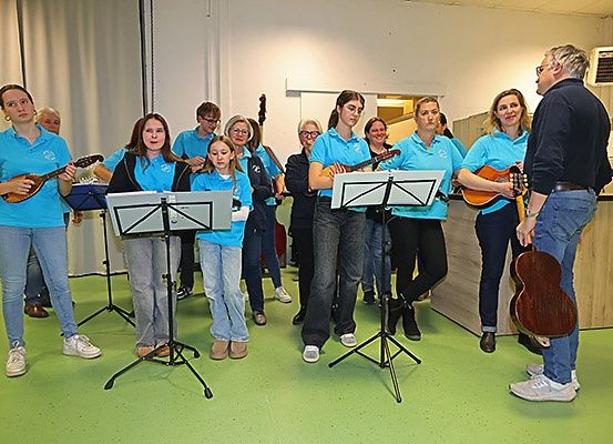 Eine Gruppe von Menschen in blauen Shirts spielt Gitarren in einem Raum. Sie stehen vor Notenständern.