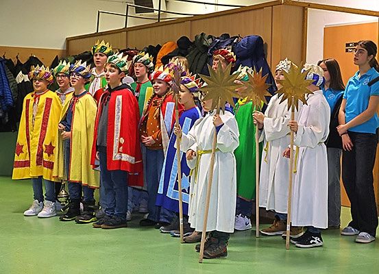 Eine Gruppe von Kindern in farbenfrohen Kostümen steht in einer Reihe und hält sternförmige Requisiten, wahrscheinlich an einer Aufführung teilnehmend.