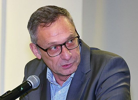 Ein Mann in Anzug und Brille spricht in ein Mikrofon bei einer Konferenz.