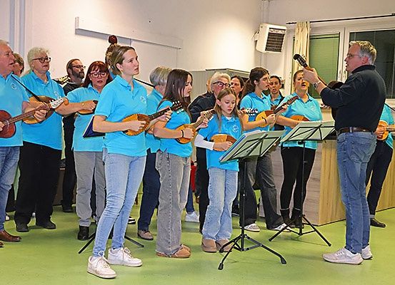 Eine Gruppe von Musikern, die blaue T-Shirts tragen, stehen in einem Raum und halten Instrumente. Ein Mann in Schwarz führt sie an.