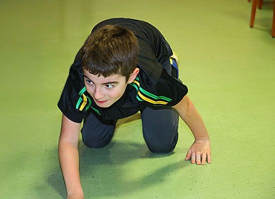 Ein junger Junge in einem schwarzen und grünen Sportshirt macht Liegestütze auf einem grünen Boden.