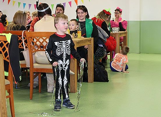 Eine Gruppe von Menschen ist in einem Raum mit Stühlen und Tischen. Einige tragen Kostüme, und ein Kind ist als Skelett gekleidet.