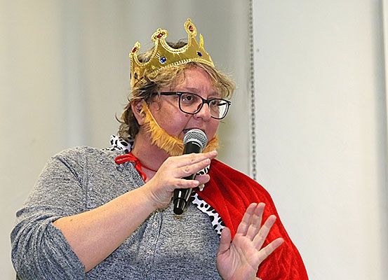 Eine Frau in einem Kostüm, die ein Mikrofon hält und eine Krone und einen falschen Bart trägt.