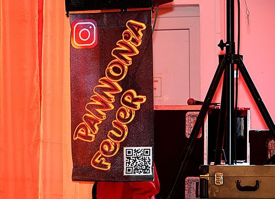 Ein Neonbanner mit den Worten "Rammpower" hängt vor einer rosa Wand, begleitet von einem Stativ und einem Mikrofon.