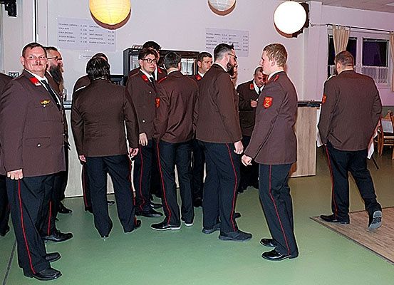 Eine Gruppe uniformierter Männer steht in einem Raum, einige schauen andere an und einer raucht.