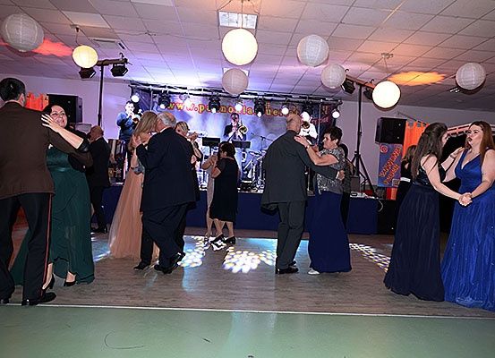 Menschen tanzen auf einer Bühne mit einer Band, beleuchtet von Scheinwerfern, unter hängenden Papierlaternen.