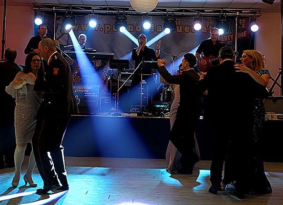 Eine Band spielt auf der Bühne mit blauen Scheinwerfern, während mehrere Paare auf der Tanzfläche tanzen.