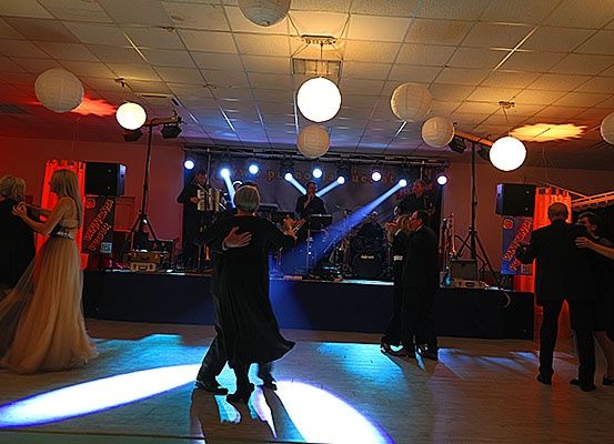 Eine Band spielt auf einer Bühne mit roten und blauen Lichtern, während Paare auf dem Boden darunter tanzen.
