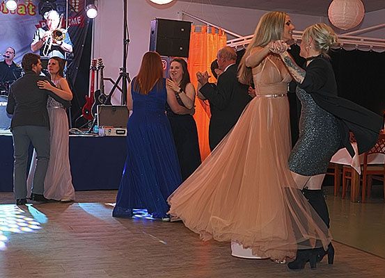 Eine lebhafte Tanzparty findet auf einer Tanzfläche mit Bühne statt. Die Leute tanzen und eine Band spielt auf der Bühne.