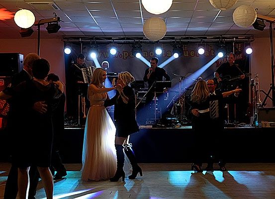 Eine lebhafte Tanzfläche mit tanzenden Menschen und einer Band, die auf der Bühne spielt. Scheinwerfer und Papierlaternen beleuchten den Bereich.