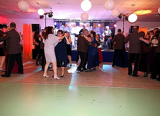 Eine Gruppe von Menschen tanzt auf einer Bühne mit roter Beleuchtung und weißen Papierlaternen, die von der Decke hängen. Eine Band spielt im Hintergrund.