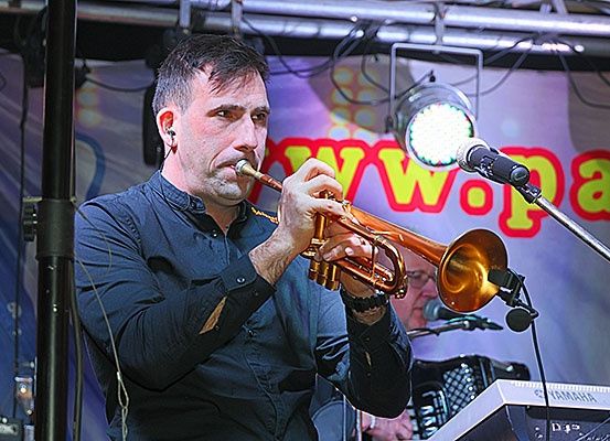 Ein Mann spielt eine Trompete auf der Bühne, hinter ihm ein Keyboard und ein Akkordeon. Vor ihm steht ein Mikrofon.