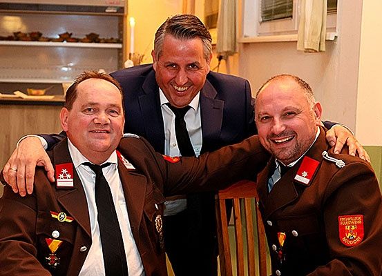 Drei Männer in Uniformen lächeln und posieren für ein Foto. Der Mann in der Mitte legt seine Hände auf die Schultern der Männer auf beiden Seiten.