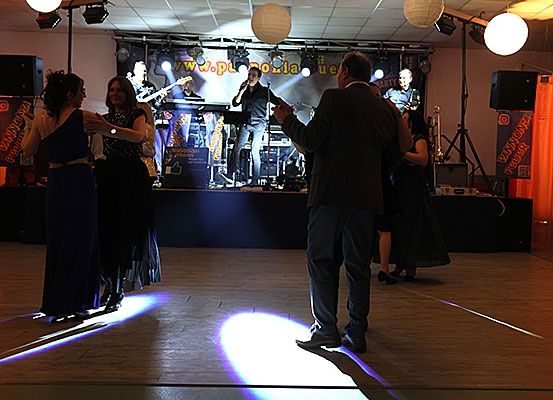 Eine Band spielt auf der Bühne mit einem Scheinwerfer auf dem Boden. Mehrere Leute tanzen auf dem Boden.