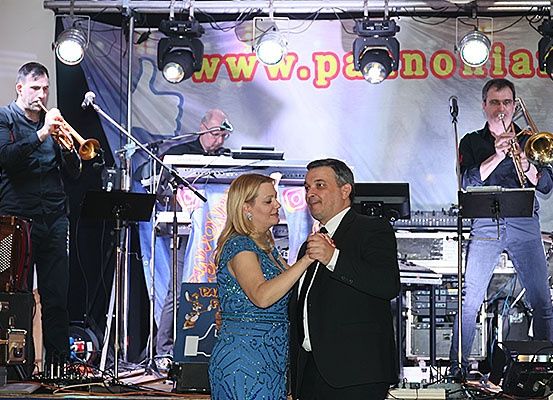 Eine Live-Band tritt auf der Bühne auf, mit einem Banner, das 'www.polonia.at' liest. Ein Mann und eine Frau tanzen im Vordergrund, während Musiker Trompeten, Keyboards und Schlagzeug spielen.