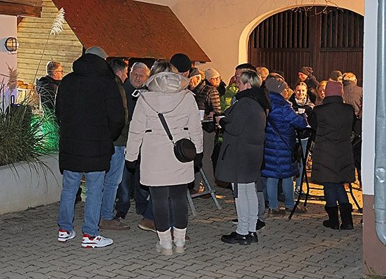 Eine Gruppe von Menschen in Winterkleidung steht nachts vor einem Gebäude, einige mit Getränken, in einer festlichen Atmosphäre.