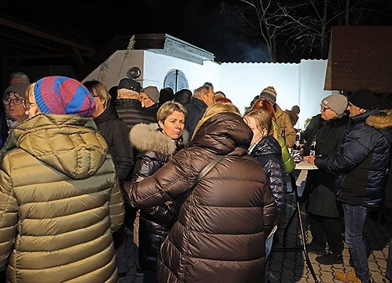 Eine Gruppe von Menschen in Winterkleidung versammelt sich nachts um ein Gebäude und unterhält sich und trinkt.