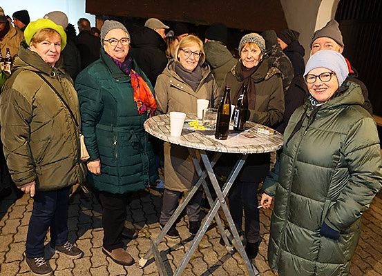 Eine Gruppe von Frauen und Männern in Winterkleidung, die bei einem Event im Freien stehen, lächeln und für ein Foto in der Nähe eines Tisches mit Flaschen und Tassen posieren.