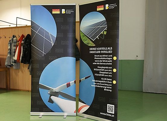 Zwei Banner sind in einem Raum ausgestellt. Die Banner zeigen Bilder von Solarmodulen und Windkraftanlagen. Der Text lautet 'Ihre Vorteile als Fanclub-Mitglied'.