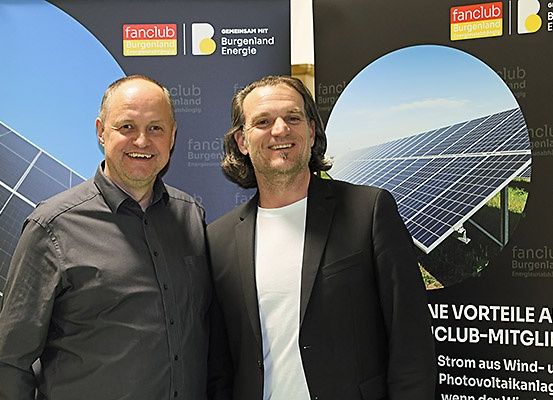 Zwei Männer stehen nebeneinander vor einem Solarpanel-Hintergrund. Ein Mann lächelt und der andere schaut in die Kamera. Hinter ihnen steht ein Schild, das 'Wir Vorteile als Club-Mitglieder' besagt.