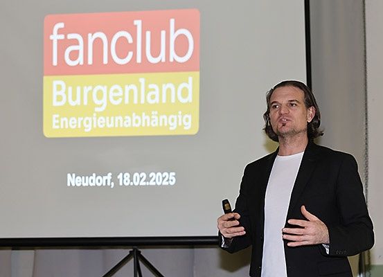 Ein Mann spricht vor einer Leinwand mit einer Präsentation zum Burgenland Fanclub.