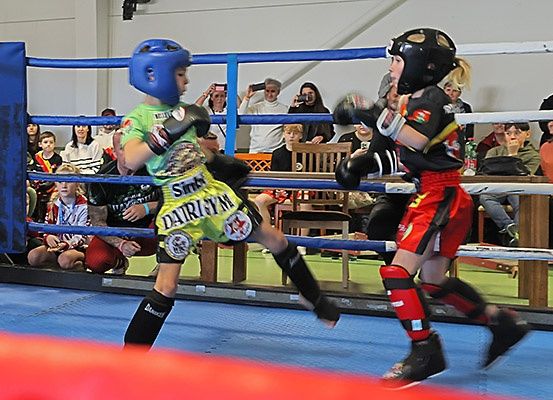 Zwei junge Boxer, einer in Grün und der andere in Rot, kämpfen in einem Ring, während Zuschauer zuschauen.