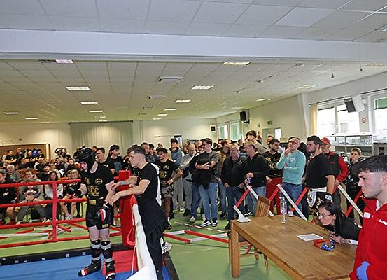 Ein Boxring-Event ist in vollem Gange mit Teilnehmern in einem Fitnessstudio, Zuschauern und Betreuern.