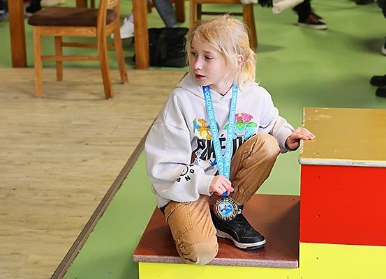 Ein junges Mädchen mit einer Medaille um den Hals sitzt auf einer Plattform in einer Turnhalle. Sie schaut nach unten, wartet möglicherweise auf ihren Zug.