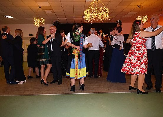 Mehrere Paare tanzen in formeller Kleidung auf einer Tanzfläche. Eine Frau in traditioneller Kleidung tanzt mit einem Mann im Anzug.