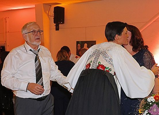 Ein älterer Mann mit Brille und Krawatte tanzt mit einer Frau in traditioneller Kleidung.