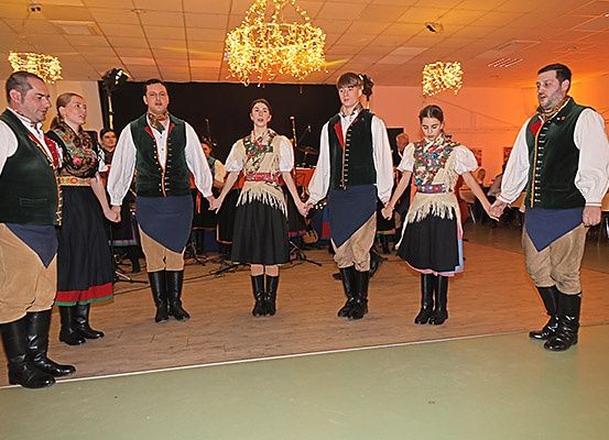 Eine Gruppe von Menschen in traditionellen Kostümen führt einen Tanz auf einer Bühne auf, an der eine Laterne hängt.