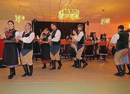 Eine Gruppe von Menschen in traditioneller Kleidung tritt auf einer Bühne auf, begleitet von einer Band im Hintergrund.