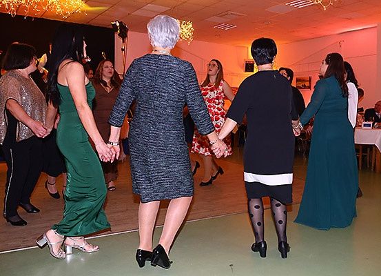 Eine Gruppe von Frauen tanzt in einem Raum mit rosa Beleuchtung. Die Frau in der Mitte trägt ein schwarzes Kleid. Eine andere Frau trägt ein rotes Kleid.