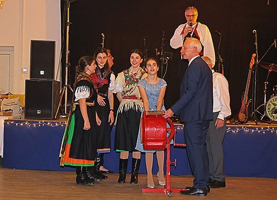 Vier Frauen in traditionellen Kostümen stehen auf einer Bühne mit einem Mann. Hinter ihnen sind Musikinstrumente und Lautsprecher aufgebaut.