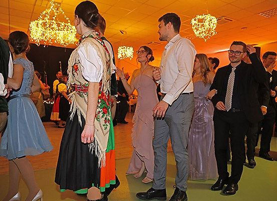 Eine Gruppe von Menschen tanzt auf einer Party. Eine Frau in traditioneller Kleidung unterhält sich mit einem Mann in formeller Kleidung.