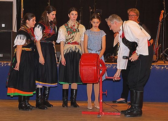 Fünf Frauen und ein Mann stehen auf einer Bühne, drei der Frauen tragen traditionelle Kleider. Der Mann bedient ein rotes Gerät.