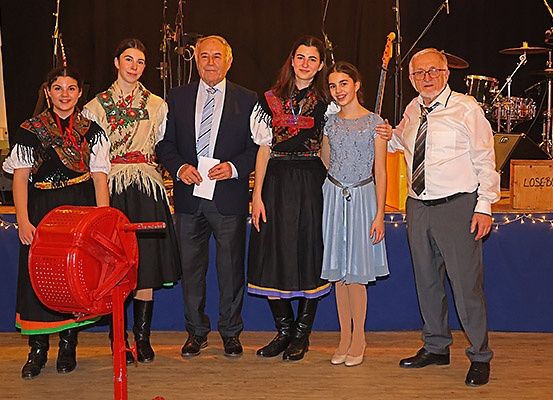 Eine Gruppe von Menschen, einschließlich eines älteren Mannes in einem Anzug, posiert für ein Foto auf der Bühne mit Musikinstrumenten im Hintergrund.